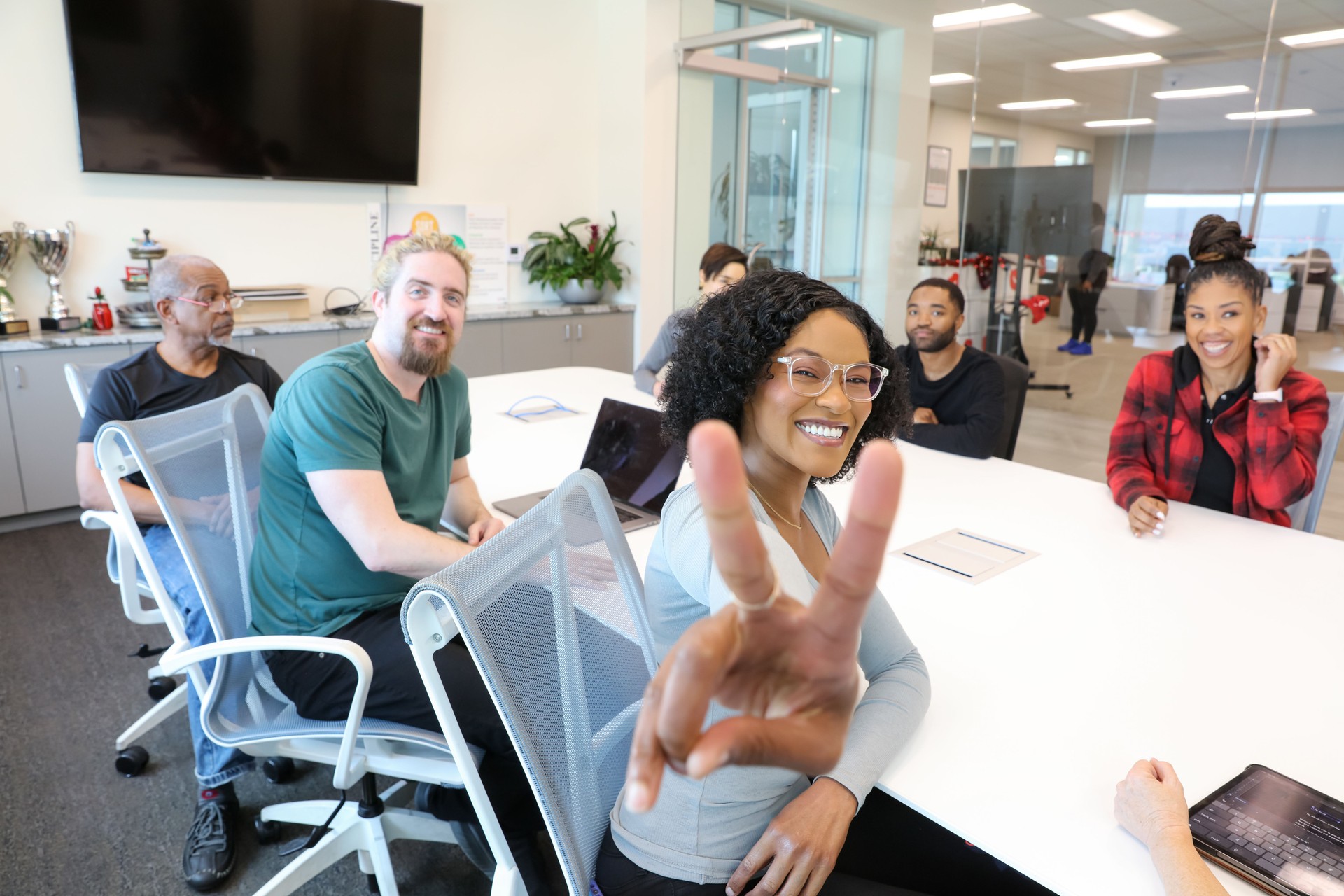 Multiracial Woman In Meeting Wearing Pair Of Glasses Makes Peace Sign